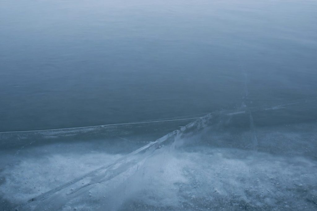 Calm water surface with a crack forming in the ice beneath